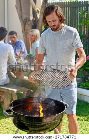 young man preparing to grill on fire for friends outdoor barbecue garden party