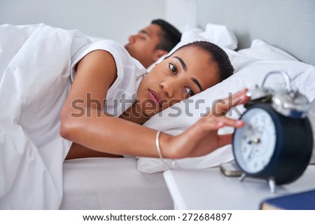 exhausted young woman waking up to alarm clock sound early morning for work