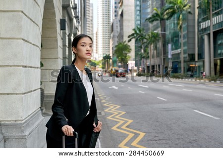 traveling asian chinese business woman waiting for taxi cab along city street sidewalk