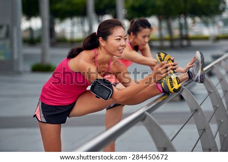 athletic asian chinese women doing stretching exercises outdoors along city sidewalk