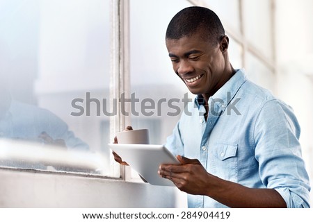 young successful black african man with morning coffee and tablet computer checking on news of investments