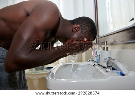 shirtless african black man washing face in basin morning in home bathroom