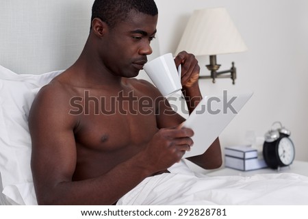 handsome african black man with tablet computer drinking coffee sitting comfortably in bed at home