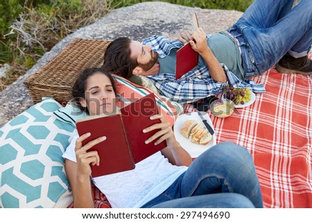 happy and relaxed couple enjoying a picnic on the rocks, near the ocean, reading a book