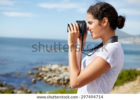 young, attractive woman standing and taking pics of the ocean using a digital camera