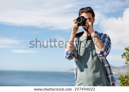 young, attractive man standing and taking pics of the ocean using a digital camera