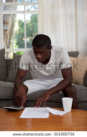 african black man sitting on sofa couch calculating home bill finances in living room