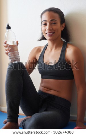 young fitness female sitting on floor with bottled water having a break from exercise routine