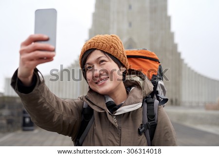 Happy travelling tourist Asian Chinese woman taking selfie in front of the Hallgrimskirkja cathedral in Reykjavik Iceland