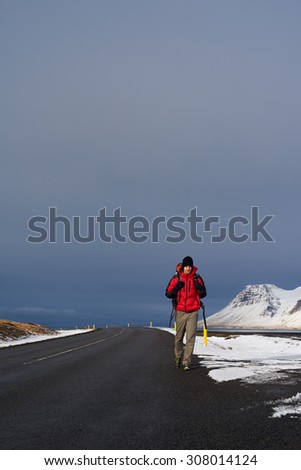 Backpacker travelling holiday on a budget hitchhiking for a ride on empty road, in harsh winter snowy cold extreme conditions