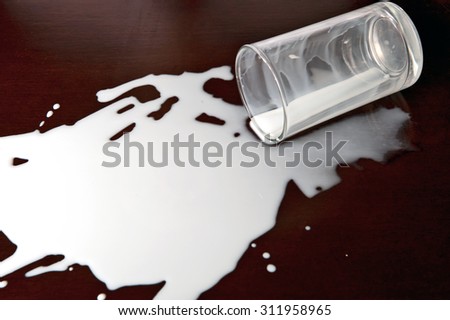 Dirty table top with knocked over glass of milk, large messy puddle of milk