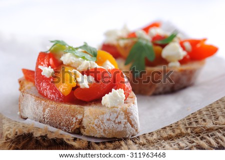 Macro shot of slices of baguette topped with roasted red and yellow peppers with feta cheese