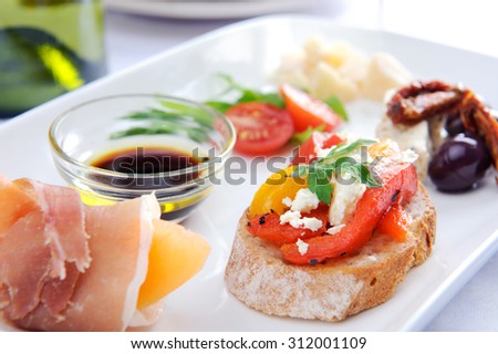 Variety of finger food on a plate; olives and sun-dried tomato, parma ham with rock melon, toast with roasted mixed peppers and feta cheese, cubes of cheese and salad