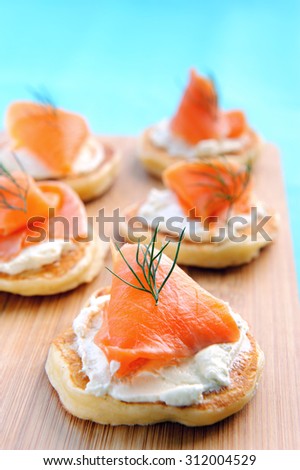 Mini pancakes blinis topped with cream cheese and smoked salmon on a wooden platter