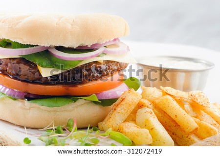 Close up on burger with thick beef patty, tomato, onion and lettuce with seasoned potato chips french fries