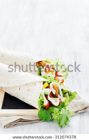 Crumbed chicken tortilla wrap with fresh healthy green salad, tomatoes, cucumber and bell peppers