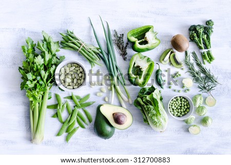 Collection of green produce from farmers market on rustic white background from overhead, broccoli, celery, avocado, brussel sprouts, kiwi, pepper, peas, beans, lettuce,