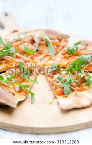 Fresh handmade thin crust pizza with rocket, roasted tomatoes and caramelised onion