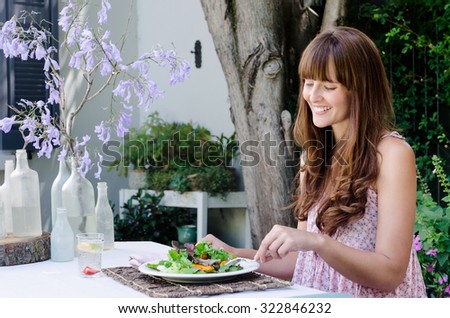 Pretty woman eating healthy green salad outdoors in garden, relaxed and happy in alfresco dining