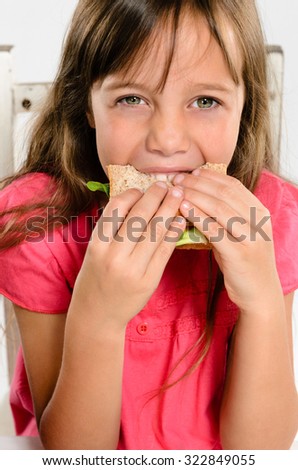 Cute young girl smiling while biting eating her wholemeal sandwich