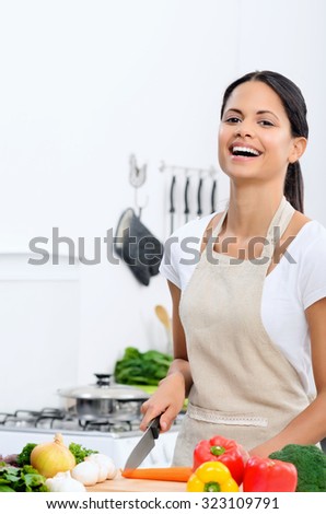 Happy mix race woman laughing while cooking and preparing food in the kitchen wearing a apron