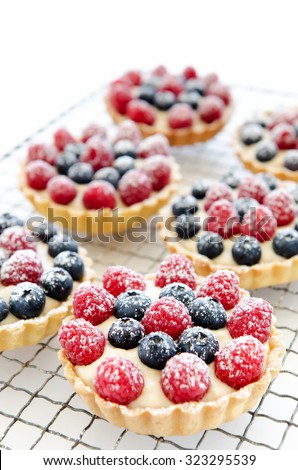 Cooling tray of raspberry and blueberry tarts sprinkled with icing sugar