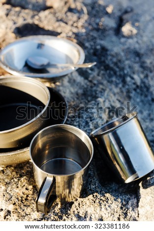 Set of camping cookware pot, bowl, pan, mug and utensils outdoor in the morning sunlight at a remote mountain wilderness campsite