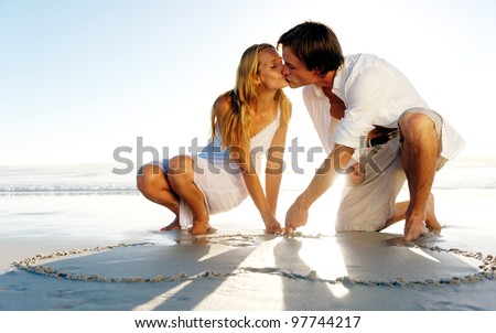 Couple draw a heart in the sand and share a romantic kiss on the beach in summer