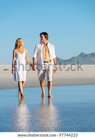 Young couple in love holding hands and taking a romantic walk along the beach during summer