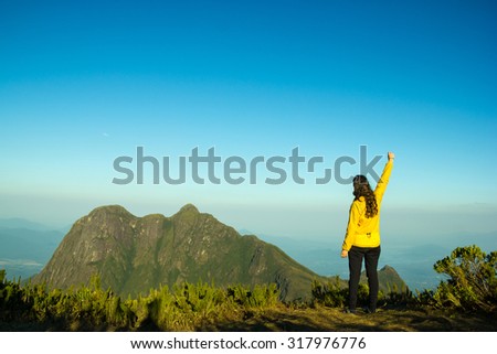Woman celebrating success on top of a mountain with one arm raised