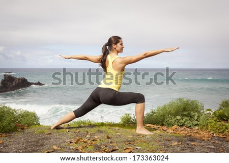 Young woman practicing yoga warrior pose near the ocean