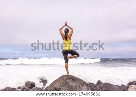Young woman practicing tree yoga pose near the ocean during sunset
