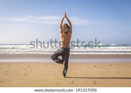 young man practicing yoga tree pose on the beach
