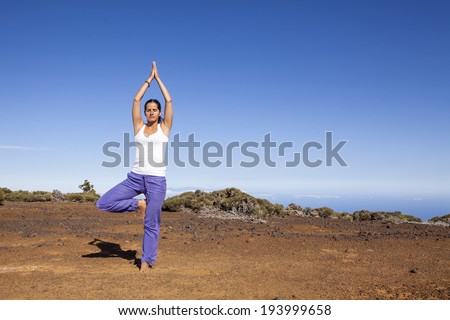 Young woman practicing tree yoga pose outdoor on a desert mountain