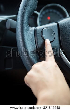 A woman hand pushes the volume control button on a steering wheel.