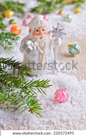 Figurine decorative Santa Claus is on the white snow in the background with fir branches and bright balls