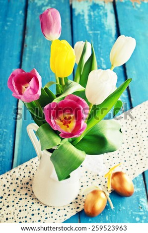 Tulips of different colors in the vase on the background of the old blue boards