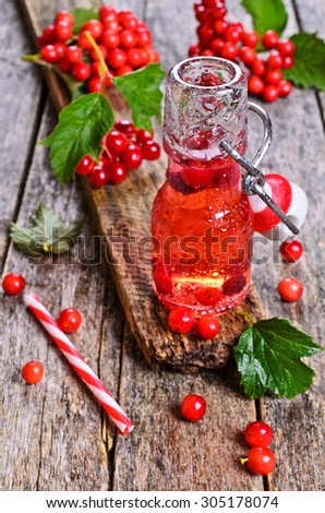Drink red in a glass container with water drops on wooden surface on the background of viburnum berries