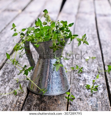 Sprigs of raw thyme with drops of water in a metal container on a wooden surface