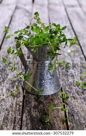 Sprigs of raw thyme with drops of water in a metal container on a wooden surface