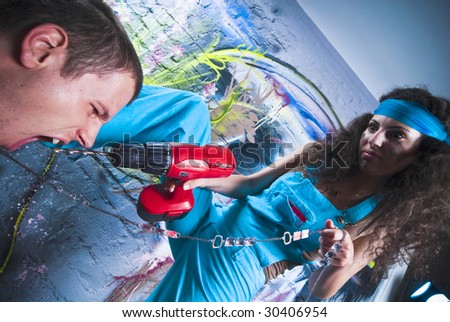 Beautiful girl and attractive boy  working at a graffiti wall. Girl using a drill press, and tyrannize the boy