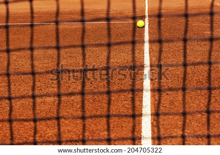 Tennis ball on tennis court. View through net. Focus on ball and part of court line. Corner of service field. Copy space available.