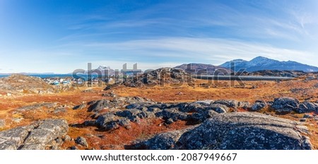 Autumn greenlandic  tundra with orange grass, stones, Inuit settlement and Sermitsiaq mountain in the background, Nuuk, Greenland