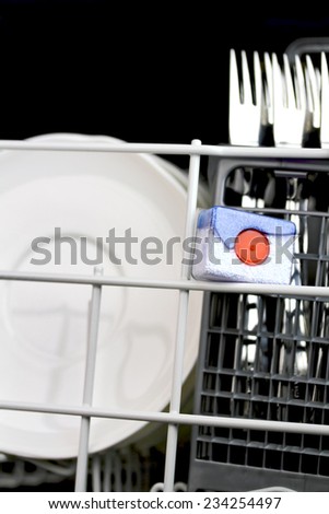 open dishwasher with clean plates in it, focus on dishwasher tabs