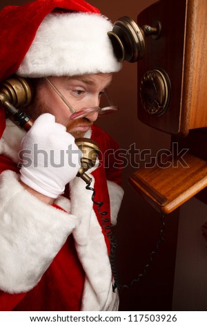 Displeased man,dressed in Santa Clause costume,is talking on the retro phone.Braun background.