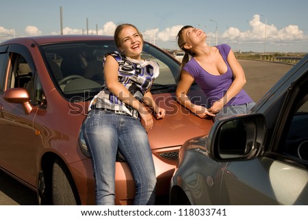 Car accident. Two young women are standing near the boonet of the smashed car and smiling.Great auto insurance or car insurance photo.