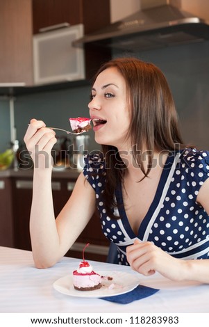 Young woman at her kitchen is eating her cake with pleasure
