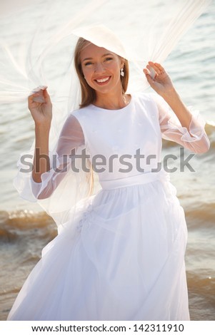 Happy bride is standing on the beach and holding her flying veil