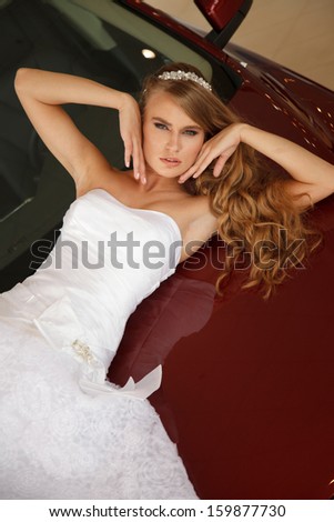 Young sensual bride lies on the  red car bonnet
