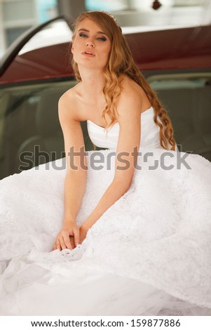 Young sensual bride sits on the  red car bonnet